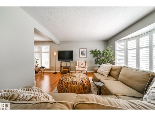 Living area featuring wood-finish flooring, bay window with plantation shutters, and a textured ceiling - 10231 46 Street, Edmonton, AB 