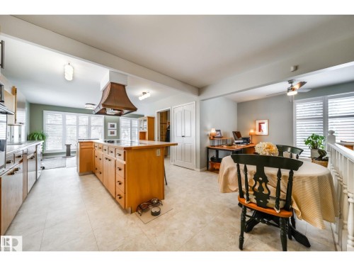 Open-concept kitchen and dining area featuring a large center island with integrated cooktop, a custom range hood, and light wood cabinetry - 10231 46 Street, Edmonton, AB 
