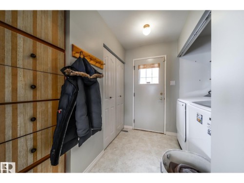 Laundry area featuring a top-load washer, a built-in wood-finish storage unit with dark hardware, and a light-colored vinyl floor - 10231 46 Street, Edmonton, AB 