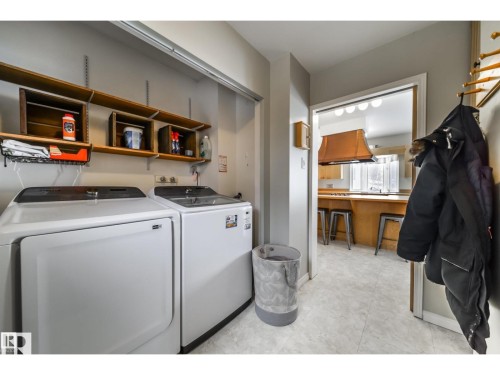 Dedicated laundry area featuring white appliances, wall-mounted wood shelving, and light-toned flooring - 10231 46 Street, Edmonton, AB 