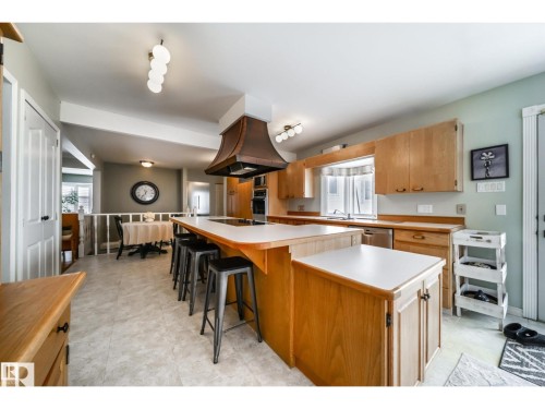 Kitchen featuring light wood cabinetry, white countertops, a large island with seating, a built-in oven, and a copper-toned range hood - 10231 46 Street, Edmonton, AB 