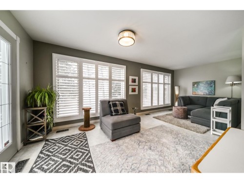 Living area featuring multiple large windows with white louvered shutters, light-toned flooring, and a decorative flush-mount ceiling light fixture - 10231 46 Street, Edmonton, AB 