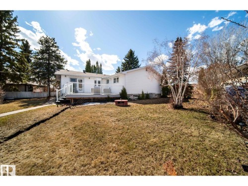 Rear exterior featuring a spacious deck with white railings, a sliding glass door entry, and mature trees - 10231 46 Street, Edmonton, AB 