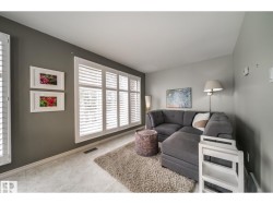 Living area featuring expansive windows with white plantation shutters, light-toned tile flooring, and neutral wall tones - 
