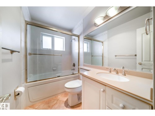 Bathroom featuring a vanity with an integrated sink and light-toned countertop, a large mirror, and a bathtub with a sliding glass enclosure - 10231 46 Street, Edmonton, AB 