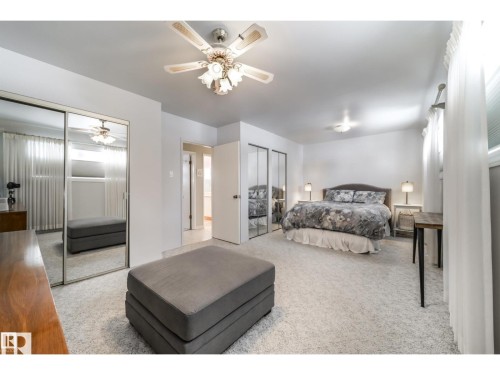 Neutral carpeted bedroom featuring a ceiling fan with integrated lighting, mirrored closet doors, and light-colored walls - 10231 46 Street, Edmonton, AB 