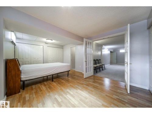 Room with wood-finish flooring, two sets of bi-fold closet doors, and French doors opening to an additional space with carpeting - 10231 46 Street, Edmonton, AB 