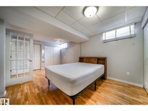 Spacious room featuring wood-finish flooring, light grey walls, and a drop ceiling - 10231 46 Street, Edmonton, AB 