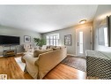 Living area featuring wood-finish flooring, a bay window with plantation shutters, a white entry door with frosted glass insert, and a flush-mount ceiling light fixture - 10231 46 Street, Edmonton, AB 