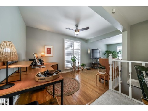 Bright interior space featuring wood-finish flooring, a contemporary ceiling fan, and white window shutters - 10231 46 Street, Edmonton, AB 
