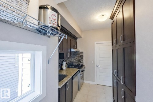 Compact kitchen featuring dark wood-finish cabinetry, granite-style countertops, stainless steel appliances, and a tiled backsplash - 1728 53 Street, Edmonton, AB - Indoor
