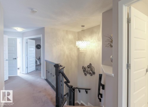 Upper landing featuring a contemporary chandelier, textured wall finish, and white panel doors - 1728 53 Street, Edmonton, AB - Indoor Photo Showing Other Room