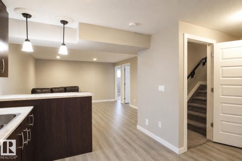 Lower level living area featuring wood-finish flooring, recessed lighting, and a built-in wet bar with a stainless steel sink and light-toned countertop - 1728 53 Street, Edmonton, AB - Indoor