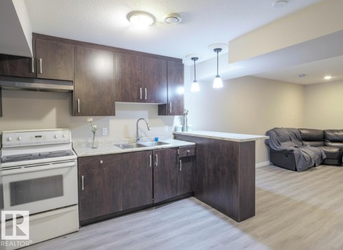 Kitchen featuring dark wood-finish cabinetry, light-toned countertops, and a full-size white range - 1728 53 Street, Edmonton, AB - Indoor Photo Showing Kitchen With Double Sink