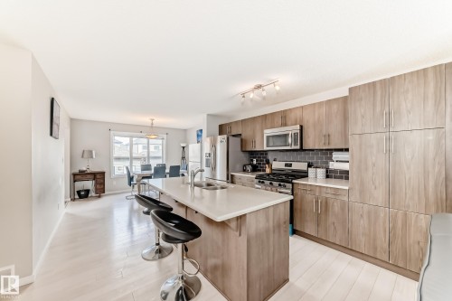 Open-concept kitchen featuring wood-finish cabinetry, stainless steel appliances, a center island with double sink, and light wood-finish flooring - 328 Watt Boulevard, Edmonton, AB - Indoor Photo Showing Kitchen With Double Sink