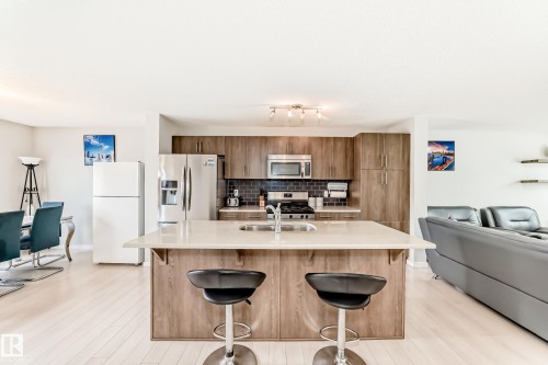 Open-concept kitchen featuring wood-finish cabinetry, stainless steel appliances, and an island with an integrated sink and light-toned countertop - 328 Watt Boulevard, Edmonton, AB - Indoor Photo Showing Kitchen With Double Sink