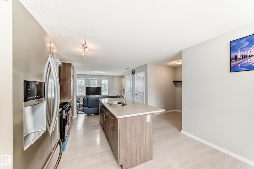 Kitchen featuring a central island with a light-toned countertop, stainless steel appliances, wood-finish cabinetry, and light wood-finish flooring - 328 Watt Boulevard, Edmonton, AB - Indoor Photo Showing Kitchen