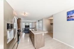 Kitchen featuring a central island with a light-toned countertop, stainless steel appliances, wood-finish cabinetry, and light wood-finish flooring - 