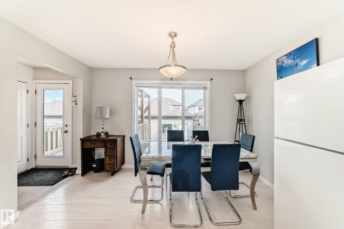 Bright dining area featuring light-finish flooring, a contemporary chandelier, a white built-in refrigerator, and a window with exterior deck access - 328 Watt Boulevard, Edmonton, AB - Indoor Photo Showing Dining Room