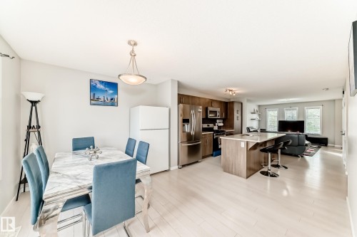 Open-concept living space featuring light wood-finish flooring, a kitchen island with seating, stainless steel appliances, and a dining area with a modern light fixture - 328 Watt Boulevard, Edmonton, AB - Indoor Photo Showing Other Room