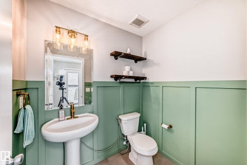 Powder room featuring green wainscoting, a pedestal sink with a brass-finish faucet, and a wall-mounted mirror with a 3-light vanity fixture - 328 Watt Boulevard, Edmonton, AB - Indoor Photo Showing Bathroom