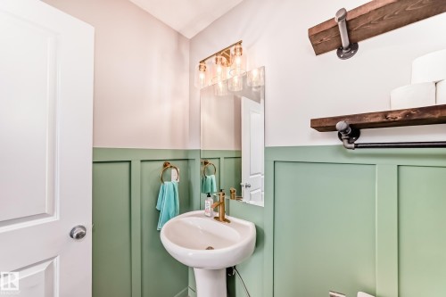 Pedestal sink with brass-finish faucet, framed by a wall-mounted mirror and a three-light vanity fixture - 328 Watt Boulevard, Edmonton, AB - Indoor Photo Showing Bathroom