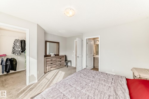 Bedroom featuring neutral wall paint, carpet flooring, a walk-in closet with wire shelving, and a door leading to a bathroom with a vanity - 328 Watt Boulevard, Edmonton, AB - Indoor Photo Showing Bedroom