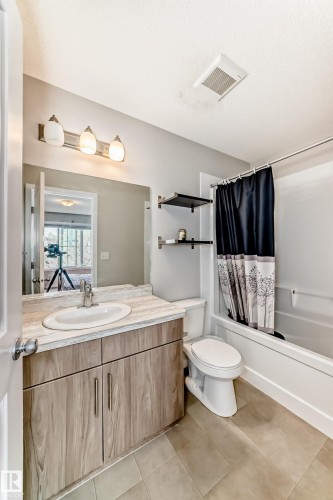 Bathroom featuring a wood-finish vanity with a single basin sink and stone-look countertop, a toilet, and a bathtub with a shower - 328 Watt Boulevard, Edmonton, AB - Indoor Photo Showing Bathroom