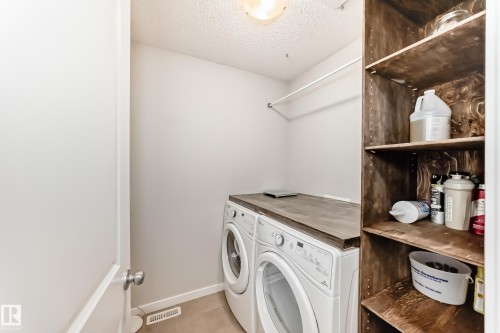 Dedicated laundry area featuring a countertop over front-load appliances, a clothes hanging rod, and integrated wood-finish shelving - 328 Watt Boulevard, Edmonton, AB - Indoor Photo Showing Laundry Room