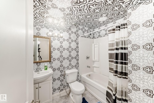 Bathroom featuring patterned wall and ceiling accents, a white vanity with integrated sink, a framed mirror, a four-bulb vanity light fixture, and a tub-shower combination with white surround - 328 Watt Boulevard, Edmonton, AB - Indoor Photo Showing Bathroom