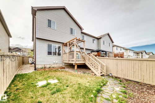 Rear exterior with light gray siding, featuring a wooden deck with railing and stairs, a wooden pergola, and a fenced yard with a stone pathway - 328 Watt Boulevard, Edmonton, AB - Outdoor With Exterior