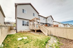 Rear exterior with light gray siding, featuring a wooden deck with railing and stairs, a wooden pergola, and a fenced yard with a stone pathway - 