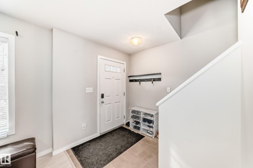 Entryway featuring a white paneled door with decorative glass, tiled flooring, a coat rack with five hooks, and light neutral wall paint - 328 Watt Boulevard, Edmonton, AB - Indoor Photo Showing Other Room