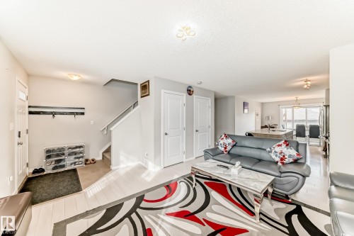 Open-concept living space with light wood-finish flooring extending into the kitchen, featuring a staircase with white risers and handrails, and a front entry door with an opaque glass insert - 328 Watt Boulevard, Edmonton, AB - Indoor