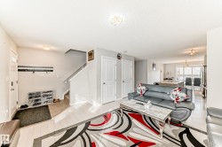Open-concept living space with light wood-finish flooring extending into the kitchen, featuring a staircase with white risers and handrails, and a front entry door with an opaque glass insert - 