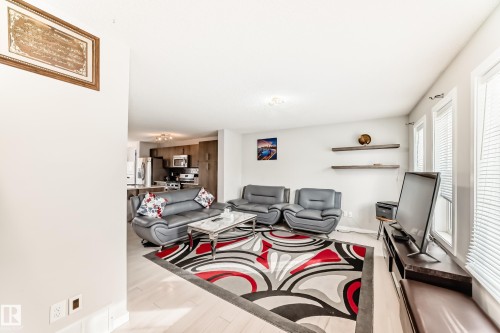 Open-concept living area with light-toned wood-finish flooring, multiple windows featuring blinds, and a kitchen visible in the background - 328 Watt Boulevard, Edmonton, AB - Indoor