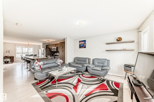 Open-concept living area featuring light wood-finish flooring, a kitchen with stainless steel appliances, and a breakfast bar with seating - 328 Watt Boulevard, Edmonton, AB - Indoor Photo Showing Living Room