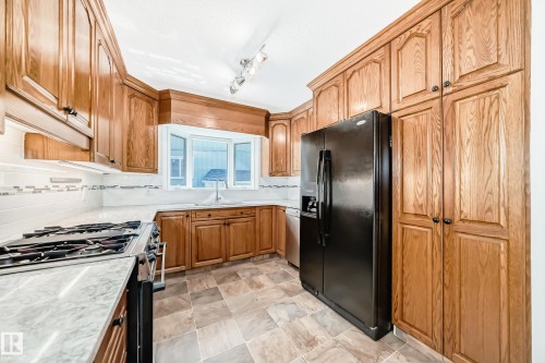 Kitchen featuring abundant wood cabinetry, a built-in refrigerator, a gas range, a bay window with a sink, and tile flooring - 79 Broadview Crescent, St. Albert, AB - Indoor Photo Showing Kitchen