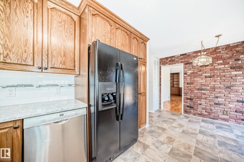 Kitchen area featuring wood cabinetry, white subway tile backsplash with decorative accent, light-colored stone countertop, and black refrigerator with ice and water dispenser - 79 Broadview Crescent, St. Albert, AB - Indoor