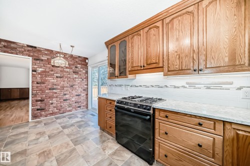 Kitchen featuring warm wood cabinetry, stone-finish tile flooring, and a subway tile backsplash with accent band - 79 Broadview Crescent, St. Albert, AB - Indoor Photo Showing Kitchen