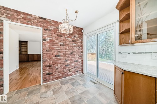 Brick accent wall with an ornate chandelier, slate-style flooring, and sliding glass doors leading to an exterior deck - 79 Broadview Crescent, St. Albert, AB - Indoor