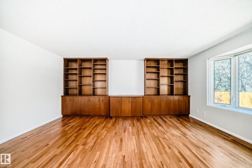 Expansive room featuring warm wood-finish flooring, built-in shelving with cabinetry, a contemporary bay window, and crisp white walls - 79 Broadview Crescent, St. Albert, AB - Indoor Photo Showing Other Room