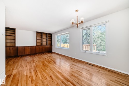 Spacious room featuring wood-finish flooring, an extensive built-in wooden shelving unit, multiple windows providing abundant natural light, and an overhead chandelier with three glass shades - 79 Broadview Crescent, St. Albert, AB - Indoor Photo Showing Other Room