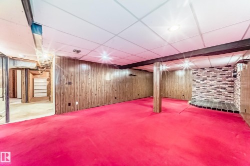 Spacious room featuring wood paneling, a drop ceiling with recessed lighting, exposed structural beams, and a brick-patterned decorative wall element - 79 Broadview Crescent, St. Albert, AB - Indoor