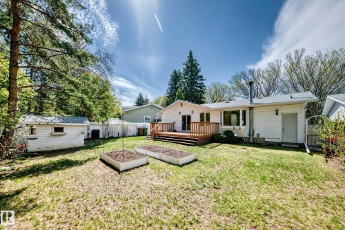 Spacious rear yard featuring a wood deck, white vinyl siding, raised garden beds, and mature trees - 79 Broadview Crescent, St. Albert, AB - Outdoor With Deck Patio Veranda