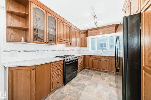 Kitchen featuring wood cabinetry, light-toned countertops, a full-size black refrigerator, and a gas range - 79 Broadview Crescent, St. Albert, AB - Indoor Photo Showing Kitchen