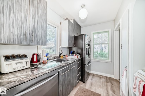 Kitchen featuring wood-finish cabinetry, stone-finish countertops, stainless steel appliances, a stainless steel sink, and wood-finish flooring - 11303 60 Street, Edmonton, AB - Indoor Photo Showing Kitchen