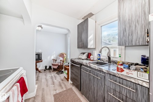 Kitchen featuring wood-finish flooring, patterned cabinetry, and a granite-look countertop with an undermount sink - 11303 60 Street, Edmonton, AB - Indoor Photo Showing Kitchen