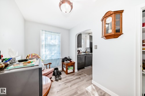 Interior room featuring light wood-finish flooring, white walls, and a window with a blue sheer curtain - 11303 60 Street, Edmonton, AB - Indoor