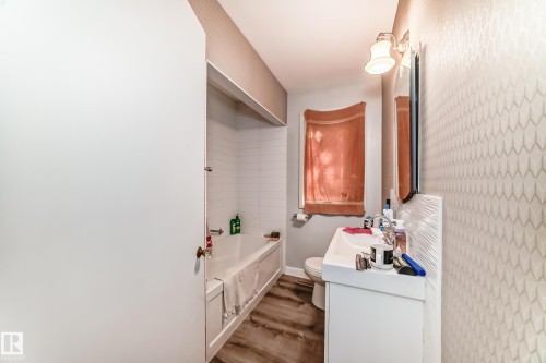 Bathroom featuring a white vanity with integrated sink, wood-finish flooring, and patterned wall covering - 11303 60 Street, Edmonton, AB - Indoor